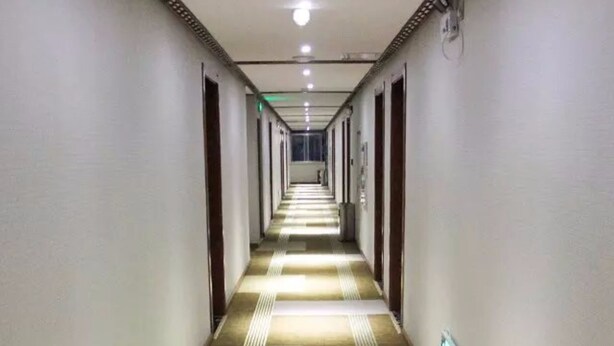 A long, narrow hotel corridor with patterned carpet, white walls, and doors on both sides. - Huangshan New Century Hotel (Huangshan)