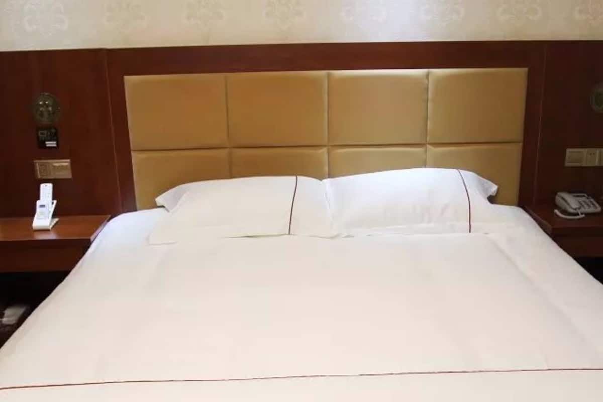 A neatly made bed with white linens, a wooden headboard, and a bedside table with a phone and a lamp.