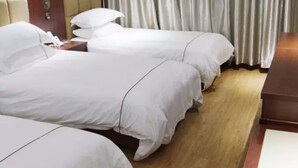 A hotel room with three single beds, wooden flooring, and a wooden nightstand with a lamp. - Huangshan New Century Hotel (Huangshan)