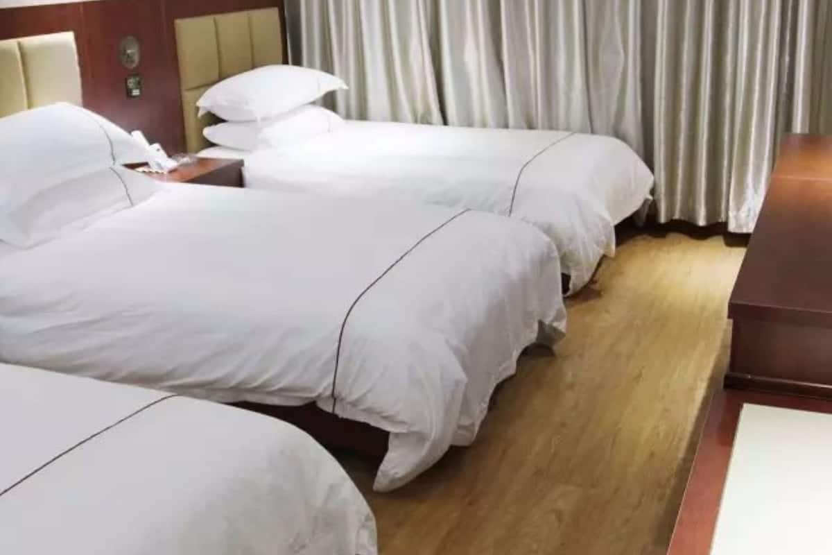 A hotel room with three single beds, wooden flooring, and a wooden nightstand with a lamp.