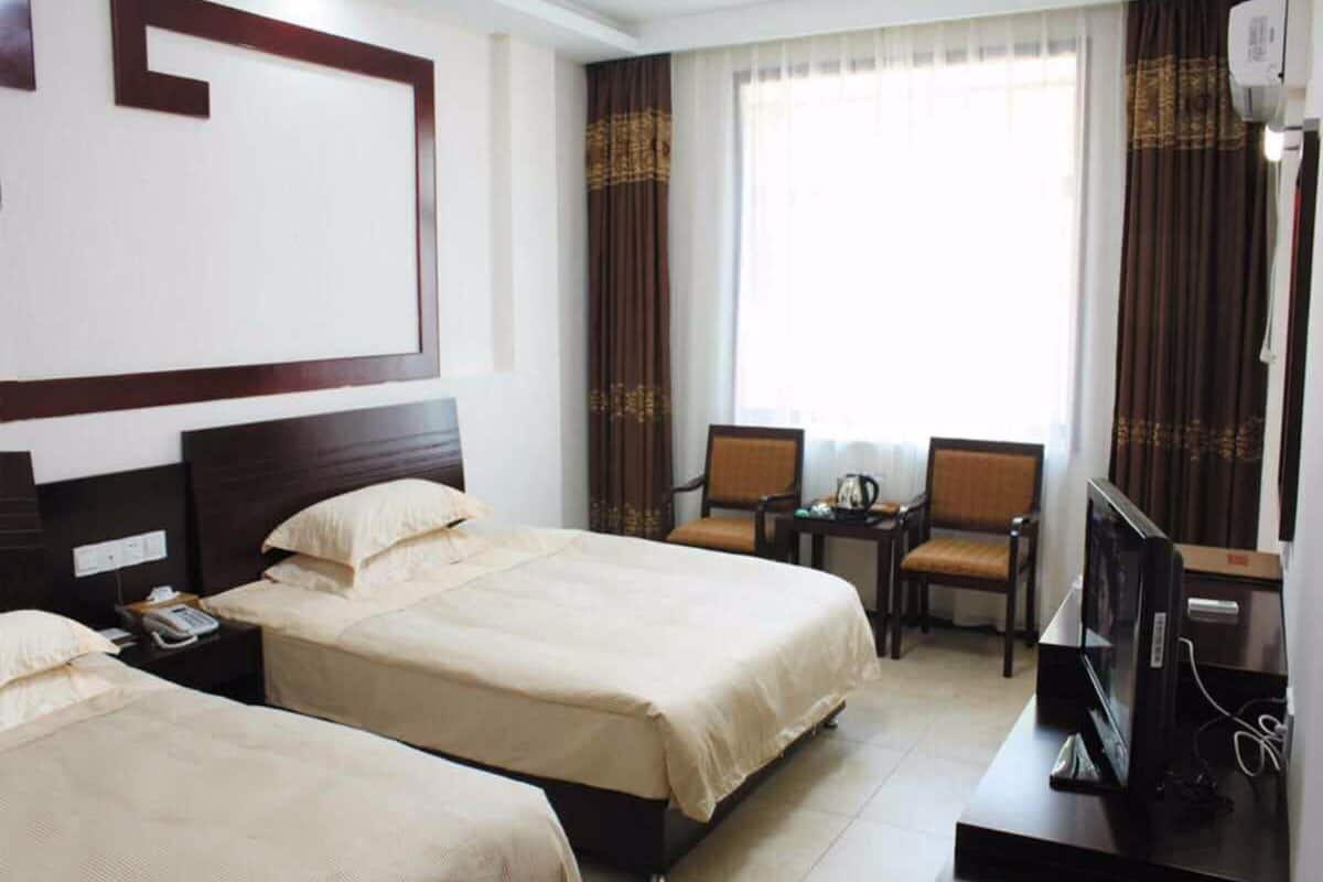Habitación de hotel con dos camas, un escritorio con una silla, un televisor y una ventana con cortinas.