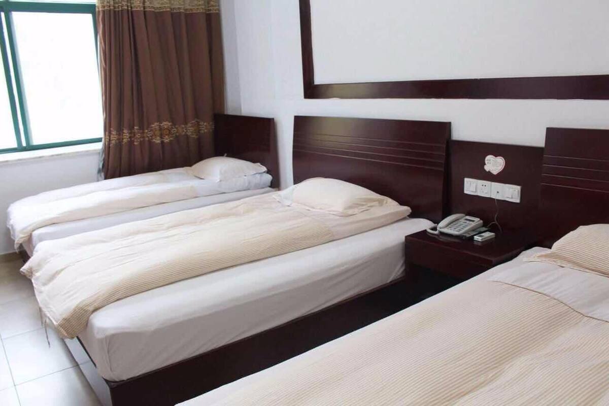 Una habitación de hotel con tres camas, un teléfono en la mesita de noche y una ventana con cortinas.