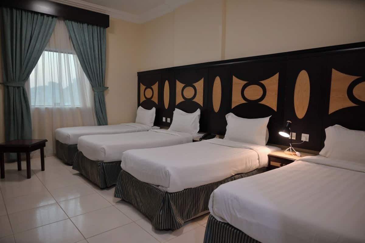 Una habitación de hotel con cuatro camas individuales alineadas, una mesita pequeña y una mesita de noche con lámpara.