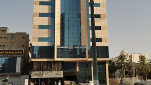 Een hoog hotel met een moderne glazen gevel, een opvallende ingang en een bord met daarop Hotel Diya Al-Mashaar.