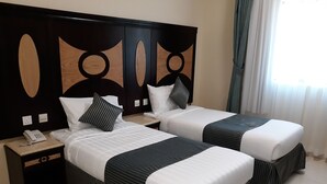 Een hotelkamer met twee bedden, een nachtkastje met telefoon, en een decoratief hoofdbord.