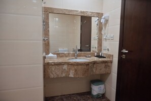 A bathroom with a marble sink, a mirror, a hairdryer, and a trash bin. - Diyar Al-Mashaer Hotel  (Makkah)
