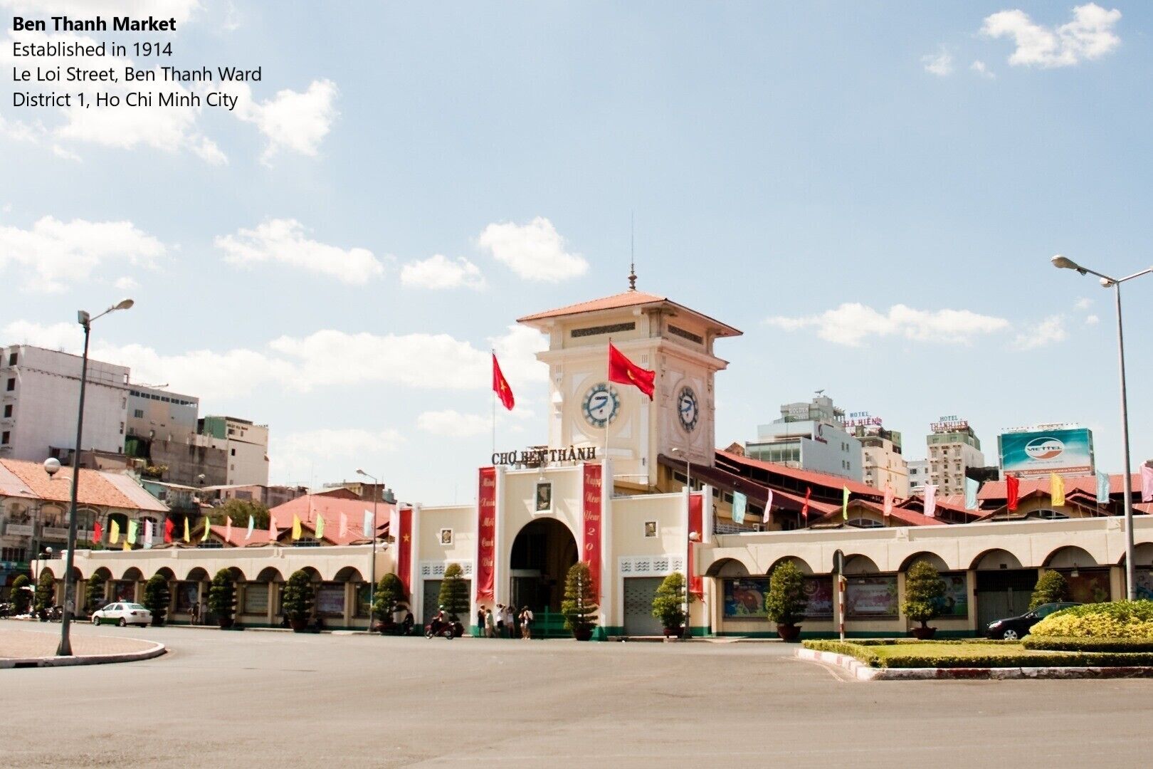 The Ben Thanh Market building with a clock tower, surrounded by other buildings and flags.