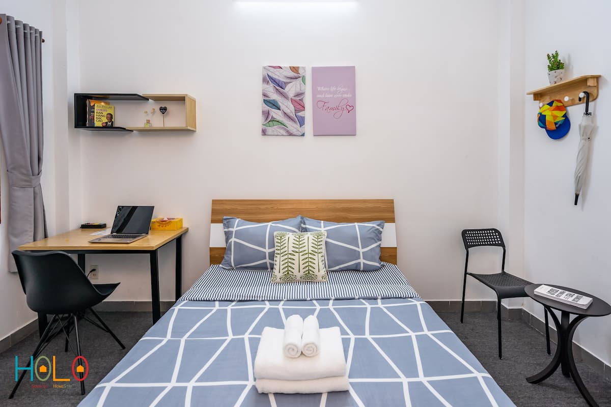A neatly arranged bedroom with a bed, a desk, a chair, and a small table.