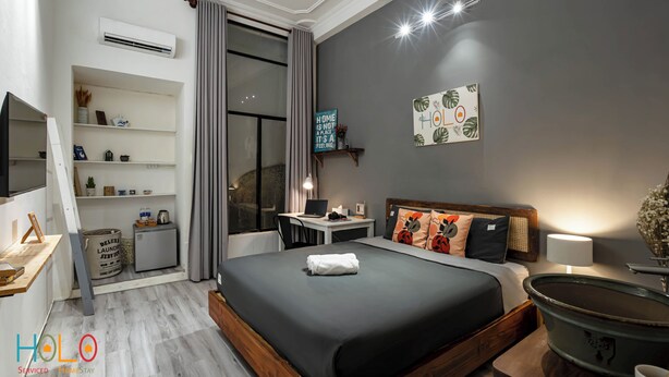 Una habitación de hotel moderna con una cama grande, un escritorio con una computadora portátil, un televisor y una ventana con cortinas.