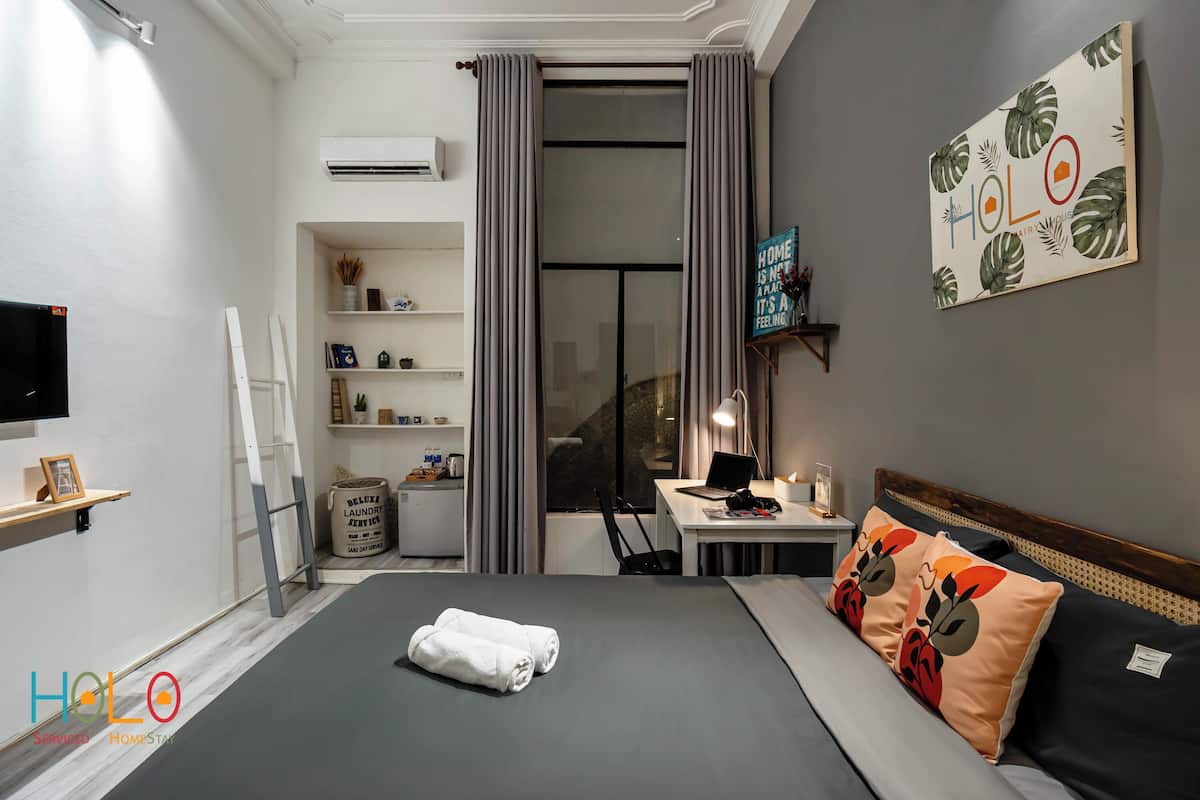 A hotel room with a bed, a desk, a chair, a TV, and a shelf with toiletries.