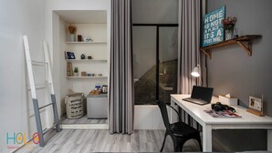 Un dormitorio moderno con cama, escritorio con computadora portátil, silla, estante con adornos y ventana con cortinas.