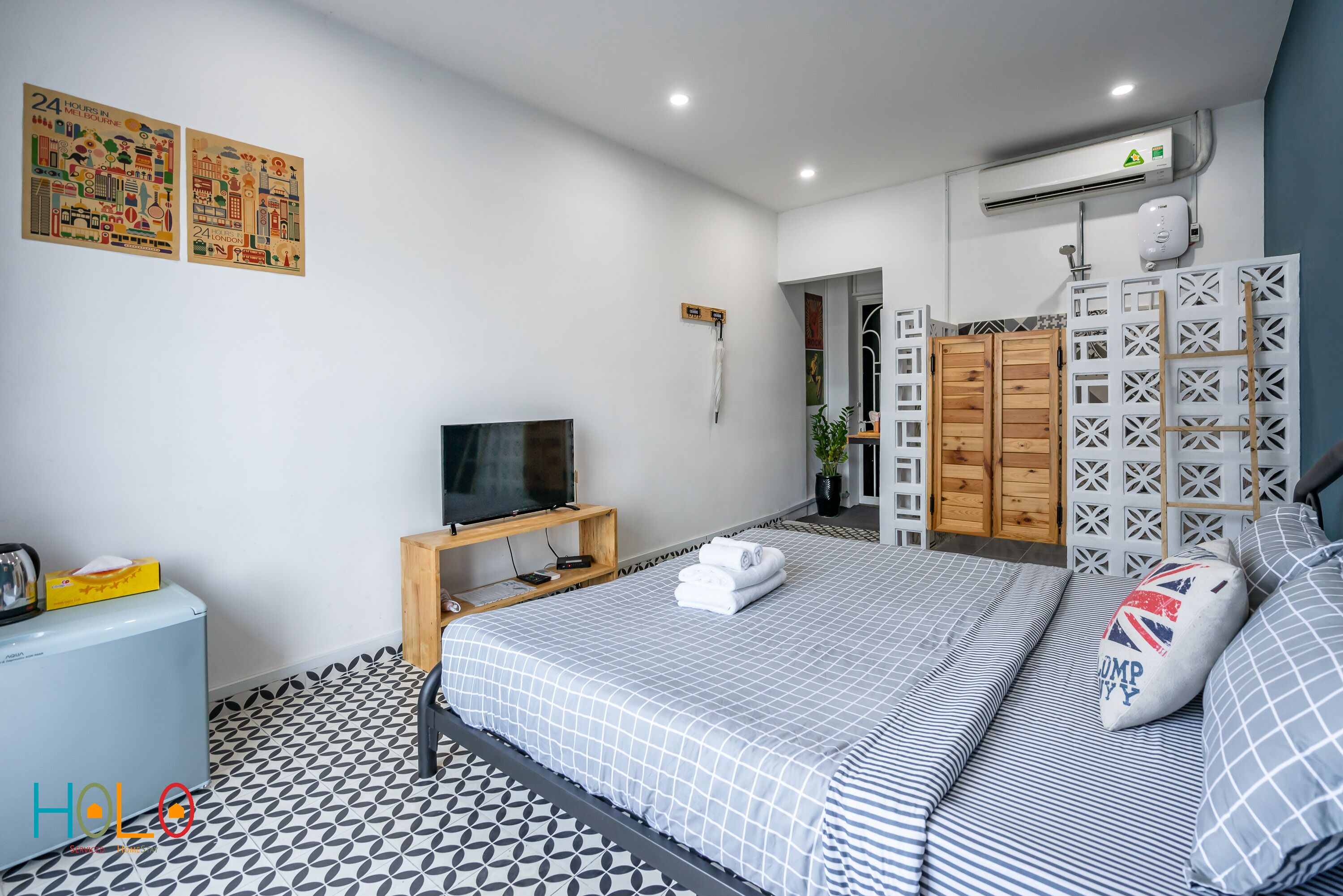 A modern hotel room with a bed, a TV, a small fridge, and a bathroom visible through an open door.