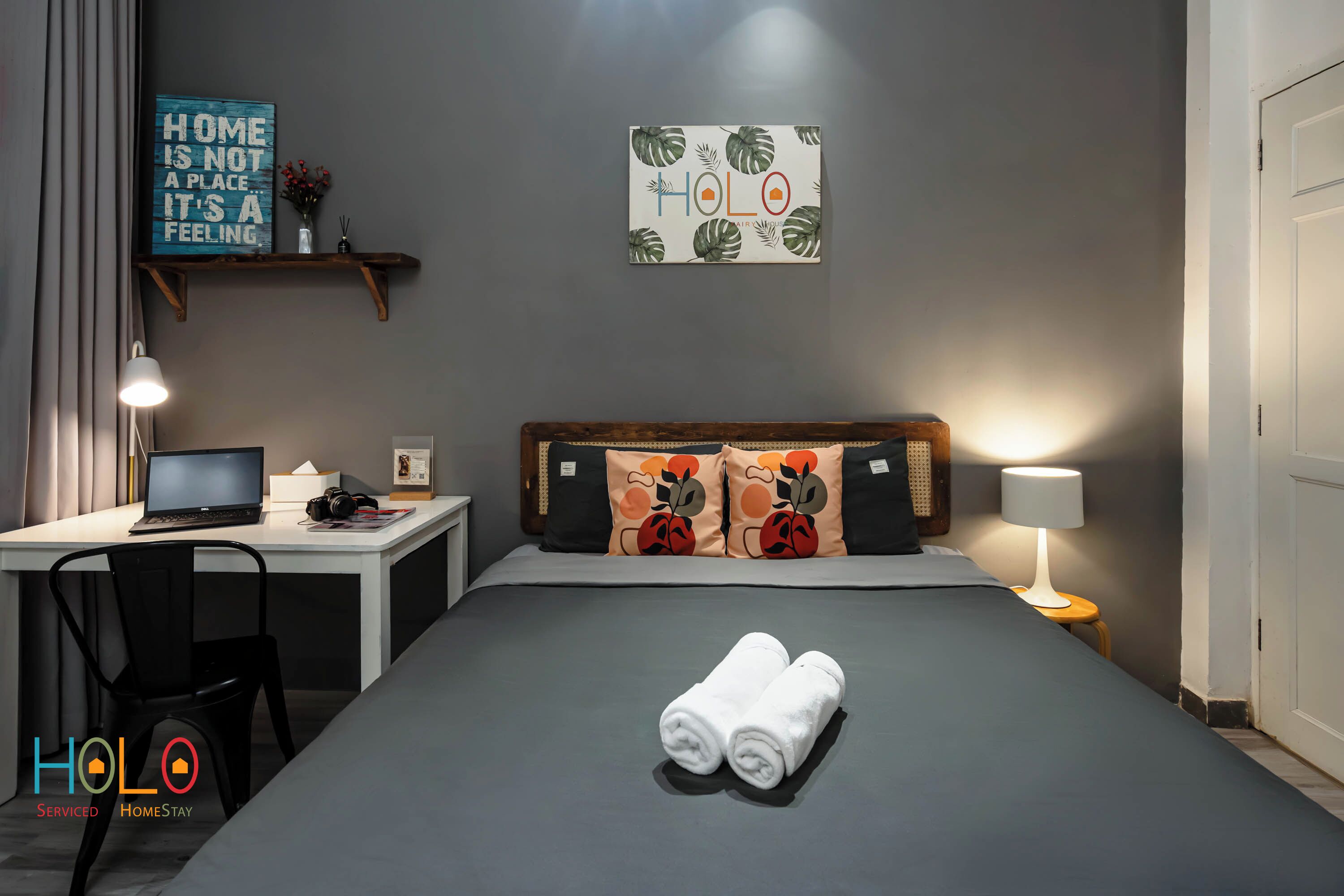 Habitación de hotel con cama, escritorio con una computadora portátil, silla, lámpara y dos toallas sobre la cama.