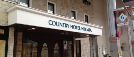 The exterior of the Country Hotel Niigata with a stone facade, large glass windows, and a sign indicating the entrance.