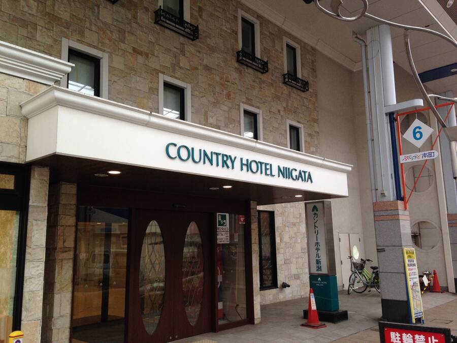 The exterior of the Country Hotel Niigata with a stone facade, large glass windows, and a sign indicating the entrance.
