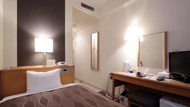 Ein Hotelzimmer mit einem Bett, einem Schreibtisch mit Computer, einem Fernseher und einem Kühlschrank.