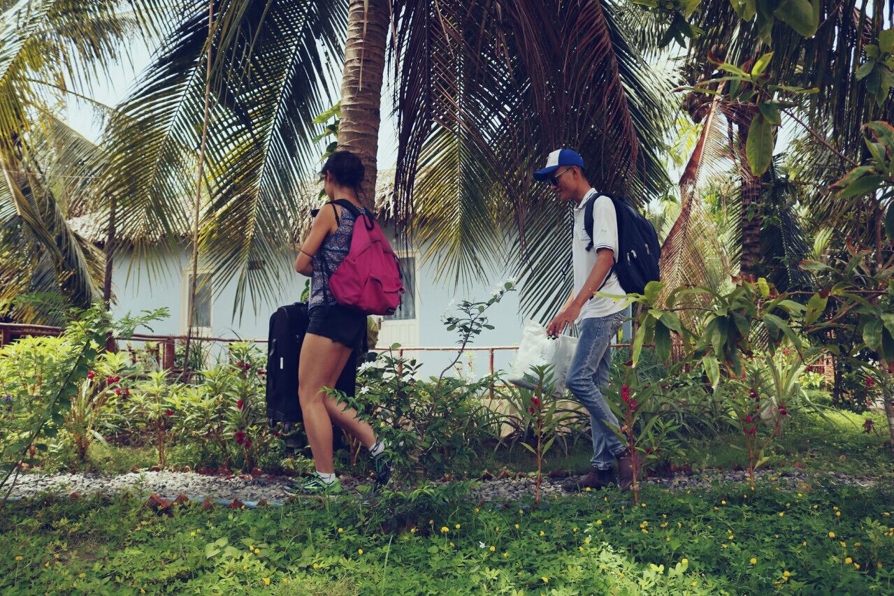 Dos personas caminando en un jardín con palmeras y diversas plantas.