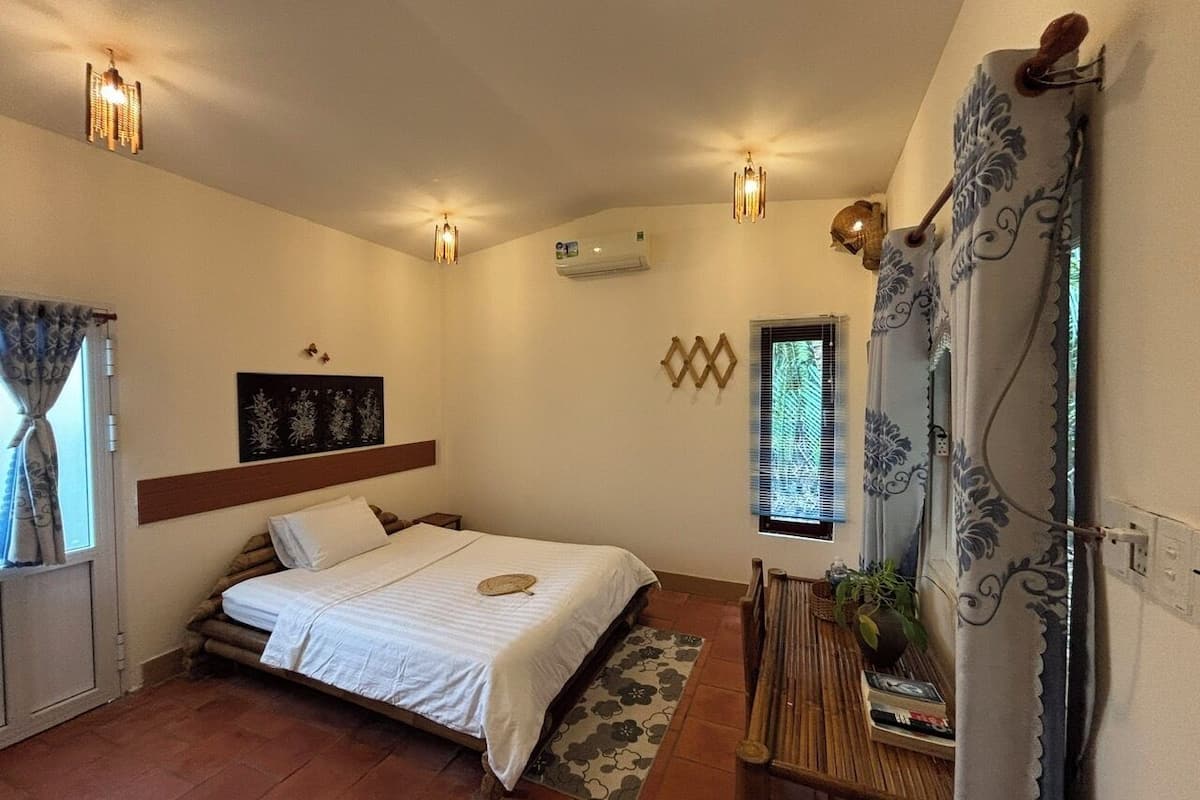 Un dormitorio con cama, mesita de noche, aire acondicionado instalado en la pared y ventana con cortinas.