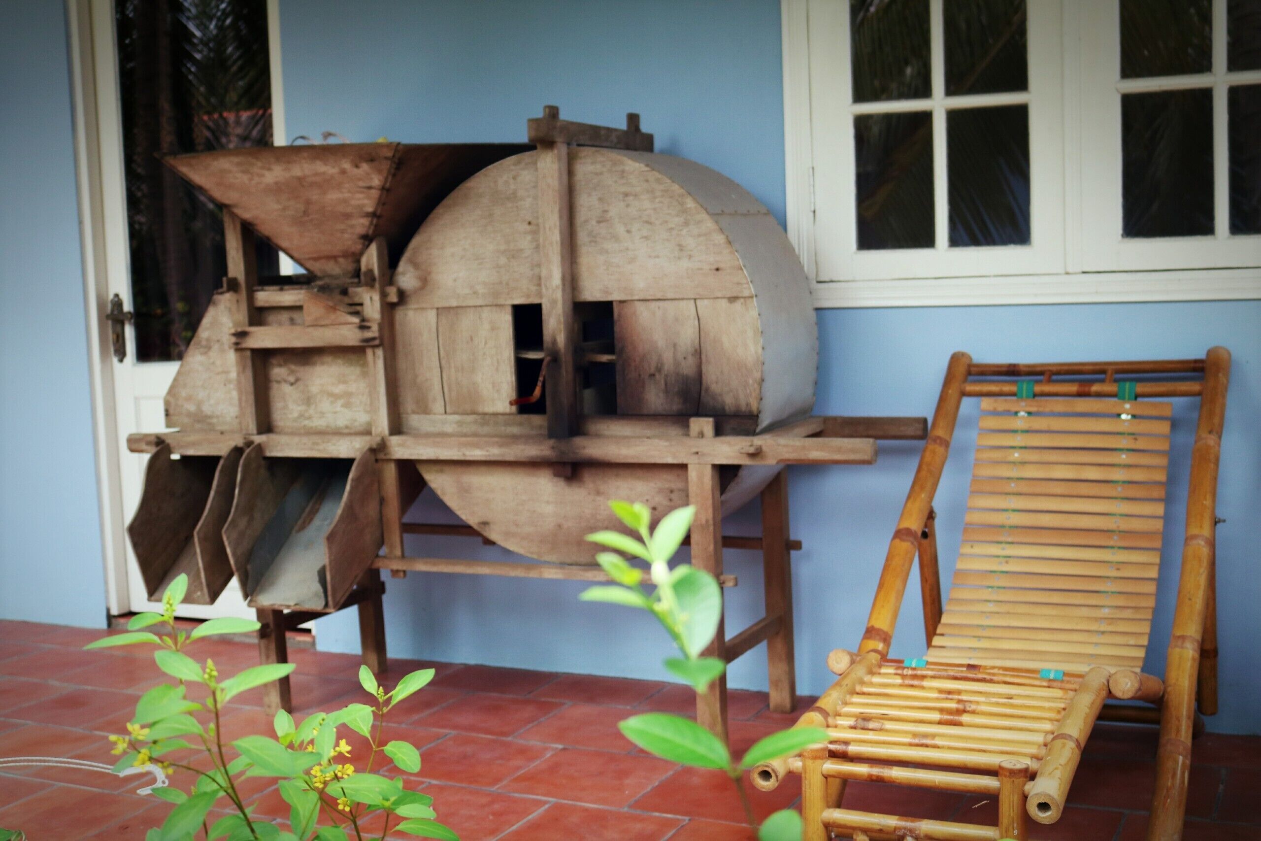 Un entorno rústico al aire libre con una estructura de madera, posiblemente una rueda hidráulica, y una silla de bambú.