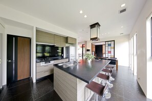 A modern kitchen with a central island, bar stools, and a large window. - Danro no yado Concept House Hoshida (Katano)