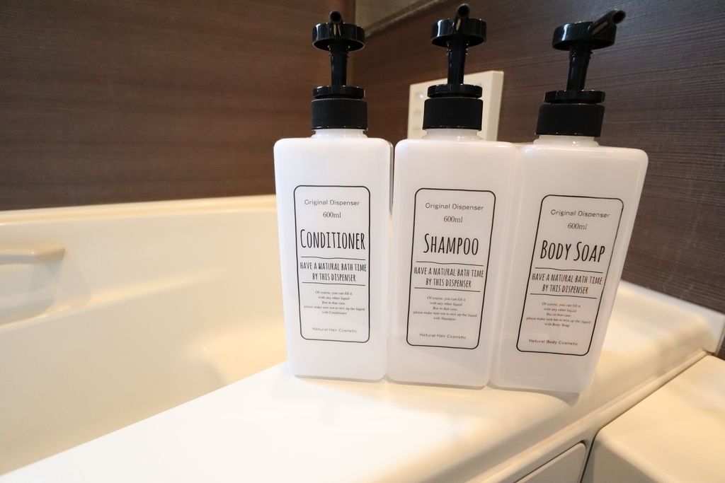 Three bottles of conditioner, shampoo, and body soap on a white surface.