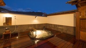 Een houten terras met een jacuzzi, een houten bankje en een kleine houten tafel met een handdoek.