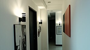 A hallway with framed artwork, wall-mounted lighting, and a door. - Transit Point Hostel Mactan Cebu (Lapu-Lapu)