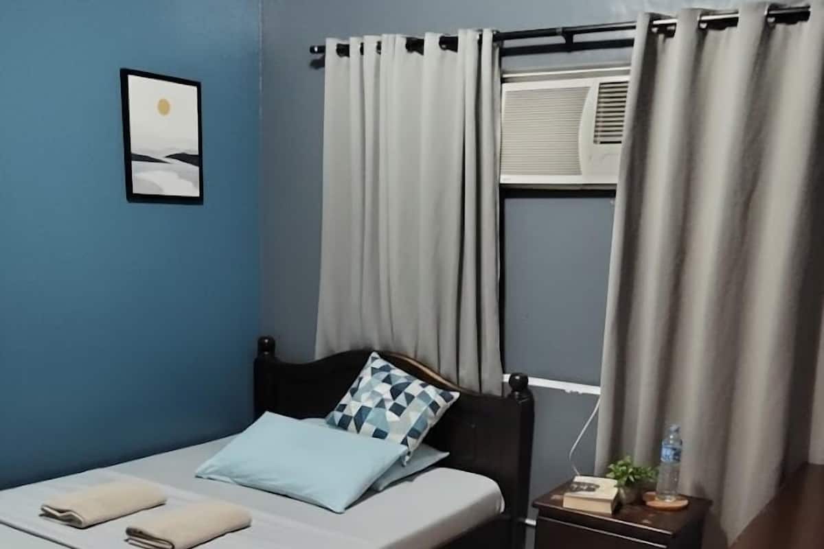 Ein Schlafzimmer mit einem Bett, einem Nachttisch, einer Kommode, einem Fenster mit Vorhängen und einer Wand-Klimaanlage.