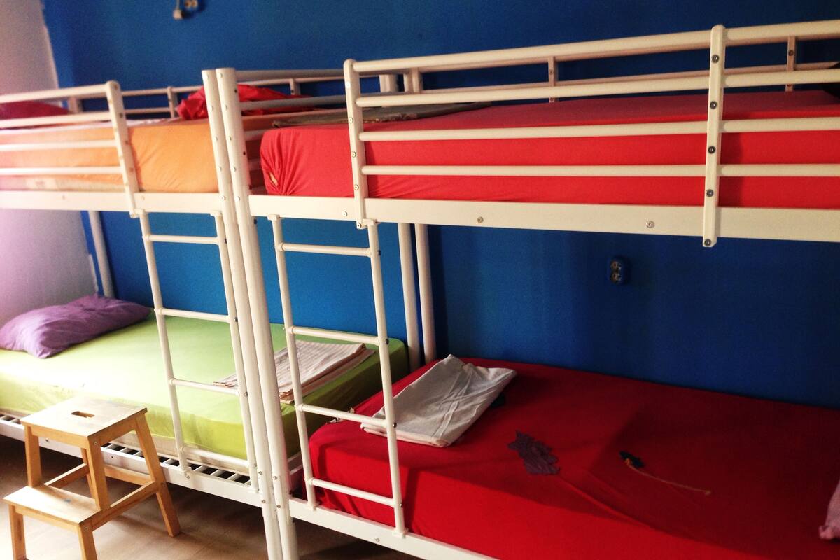 A bunk bed room with a small wooden stool and a purple pillow.