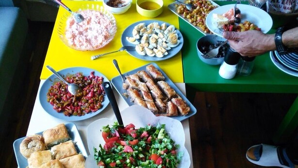A dining table with various dishes, a sofa, and a person eating. - Shantihome Hostel (Izmir)