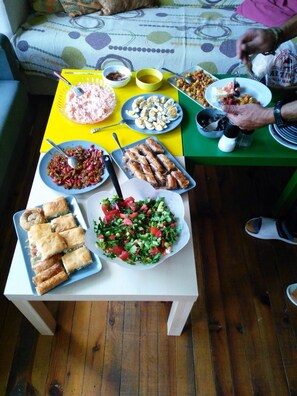 A dining table with various dishes, a sofa, and a person eating. - Shantihome Hostel (Izmir)