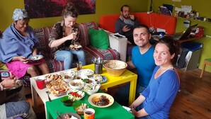A group of people sitting on a couch and a table with various dishes, suggesting a casual dining setting. - Shantihome Hostel (Izmir)