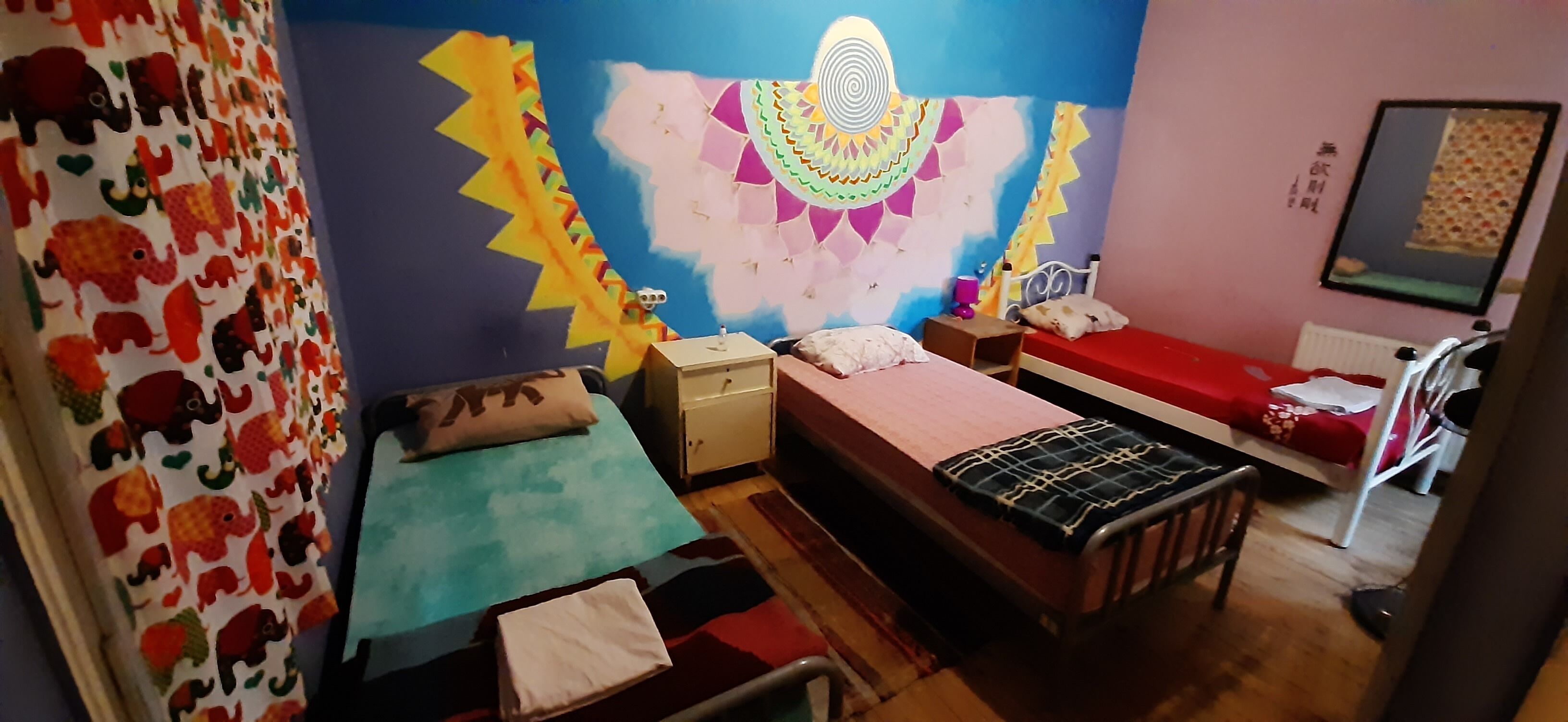Una camera da letto con due letti, un comodino, un tavolino e un murales colorato.