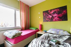A room with two beds, a window with curtains, a wall with a space-themed painting, and a radiator. - Shantihome Hostel (Izmir)