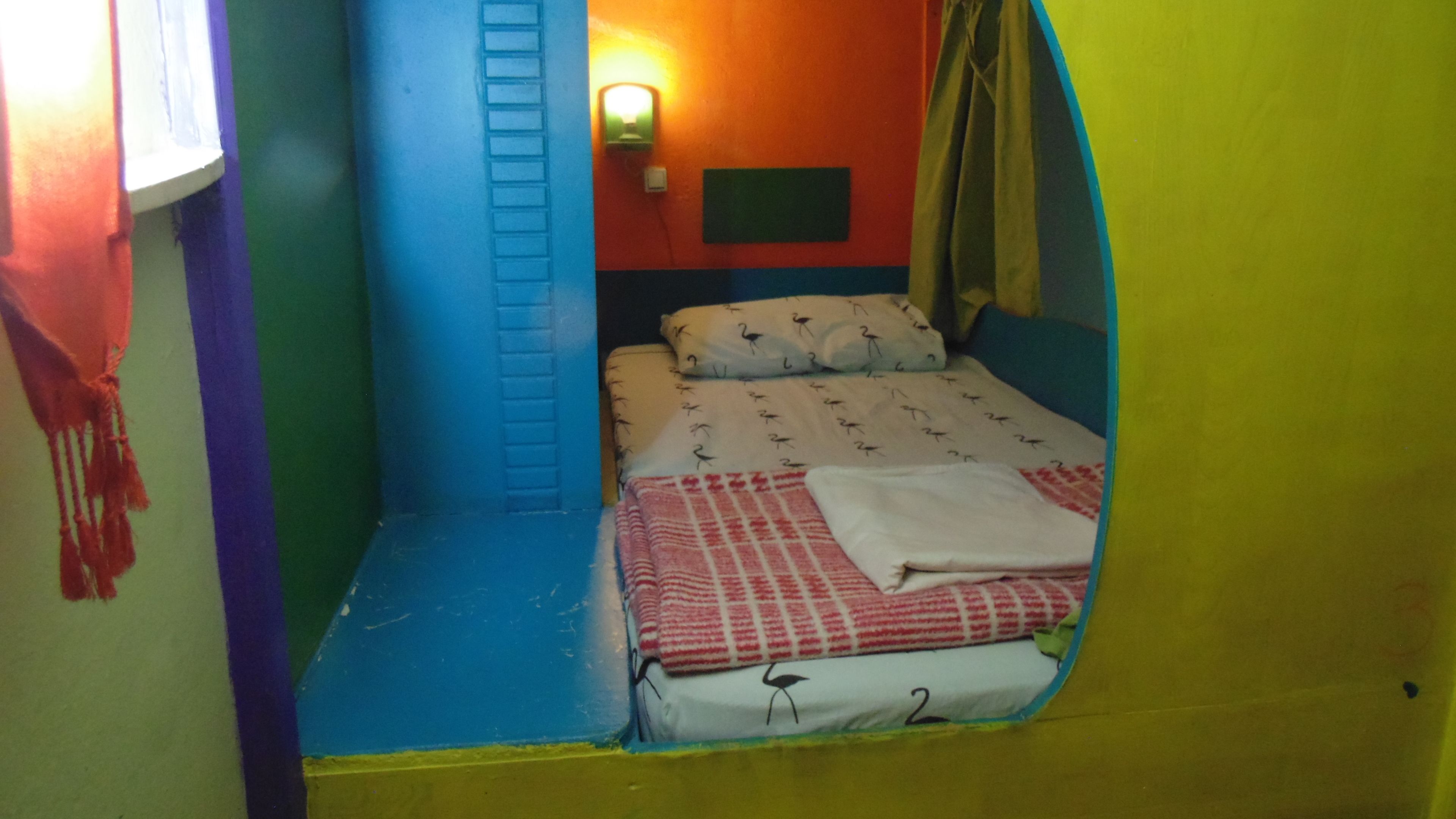 Une petite pièce colorée, avec un lit, une échelle et une lampe fixée au mur.