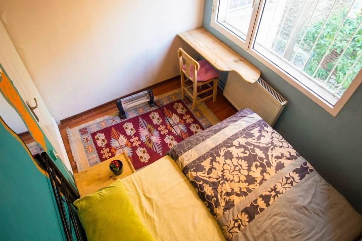 A small room with a window, a radiator, a wooden bench, a chair, and a patterned rug.