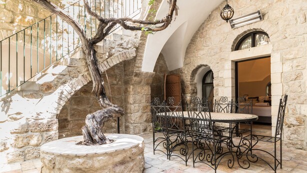 Un patio de piedra con una mesa redonda y sillas, una escalera y vista al interior.