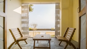 An open patio with two wooden benches and a table, leading to a view of the sea.