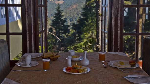 A table set for breakfast with a mountain view, including plates of food, a vase, and a glass of juice.