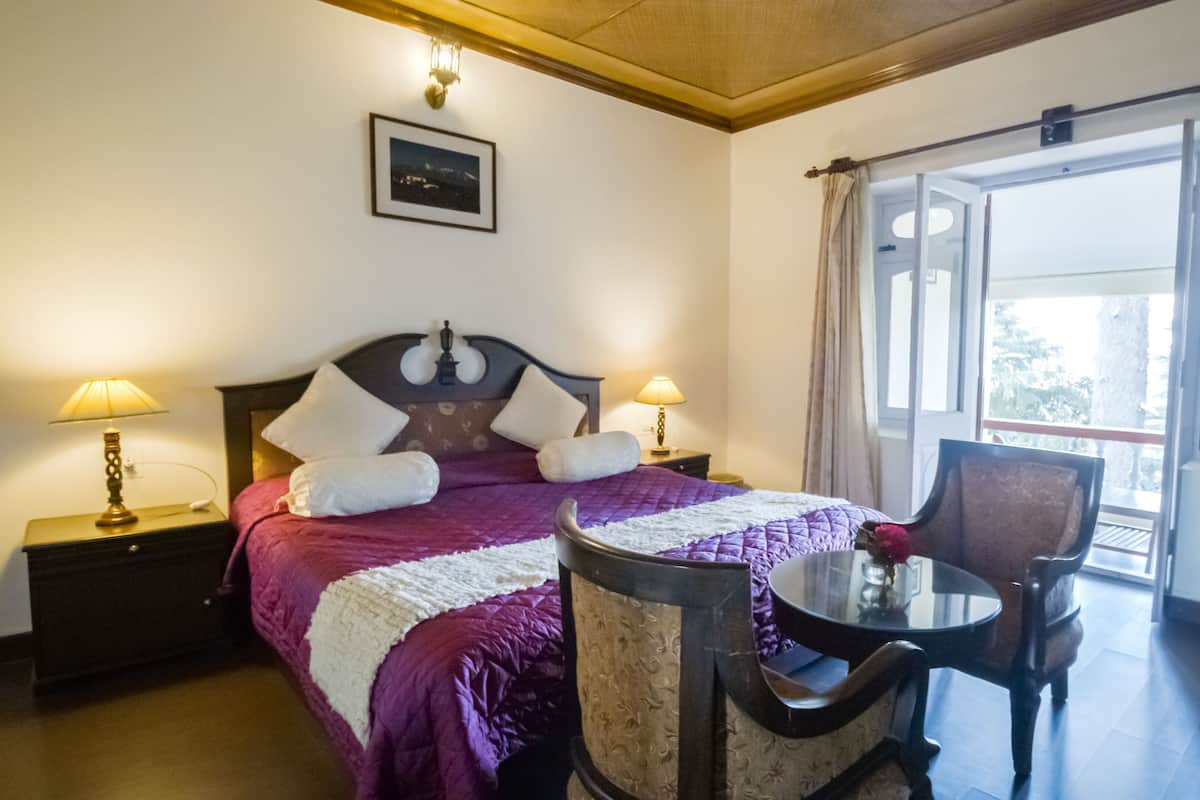 Une chambre d’hôtel avec un lit, deux lampes de chevet, une chaise, une petite table et une fenêtre avec des rideaux.