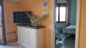 A room with a white cabinet, a flat-screen TV, and a window with curtains.