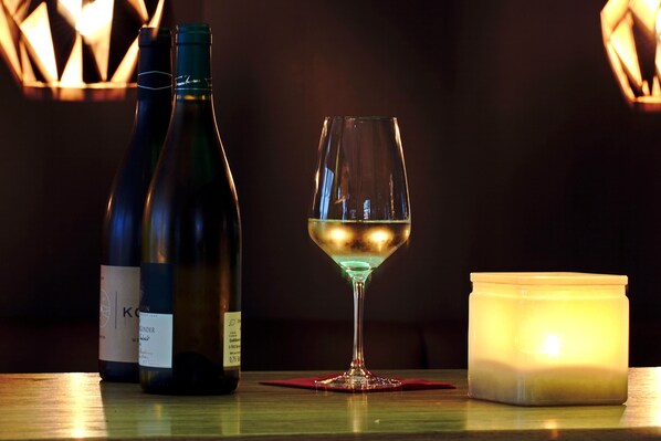 Duas garrafas de vinho e um copo sobre uma mesa com uma vela acesa.