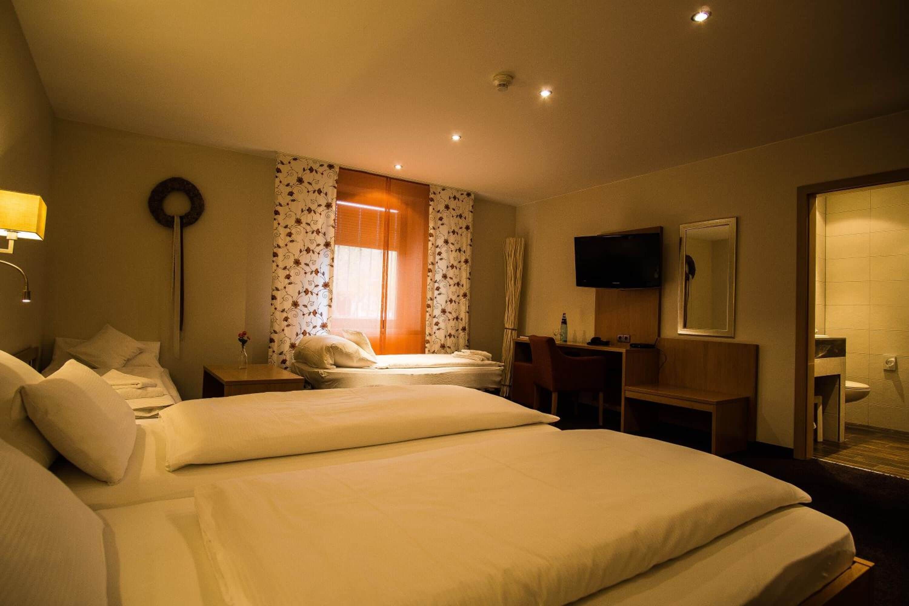 A hotel room with two beds, a desk, a television, and a bathroom.