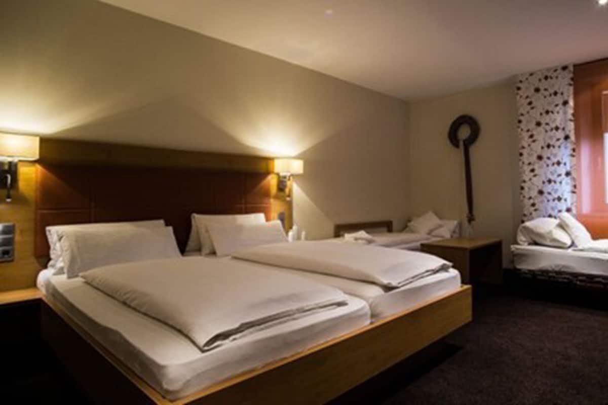 Habitación de hotel con dos camas, cabecera de madera, mesita de noche y ventana con cortinas.