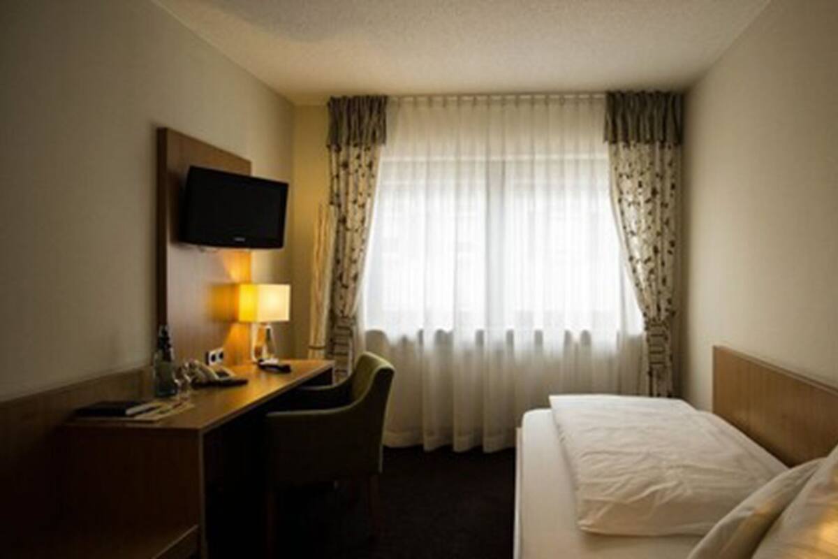 Habitación de hotel con cama, escritorio, silla, televisor y ventana con cortinas.