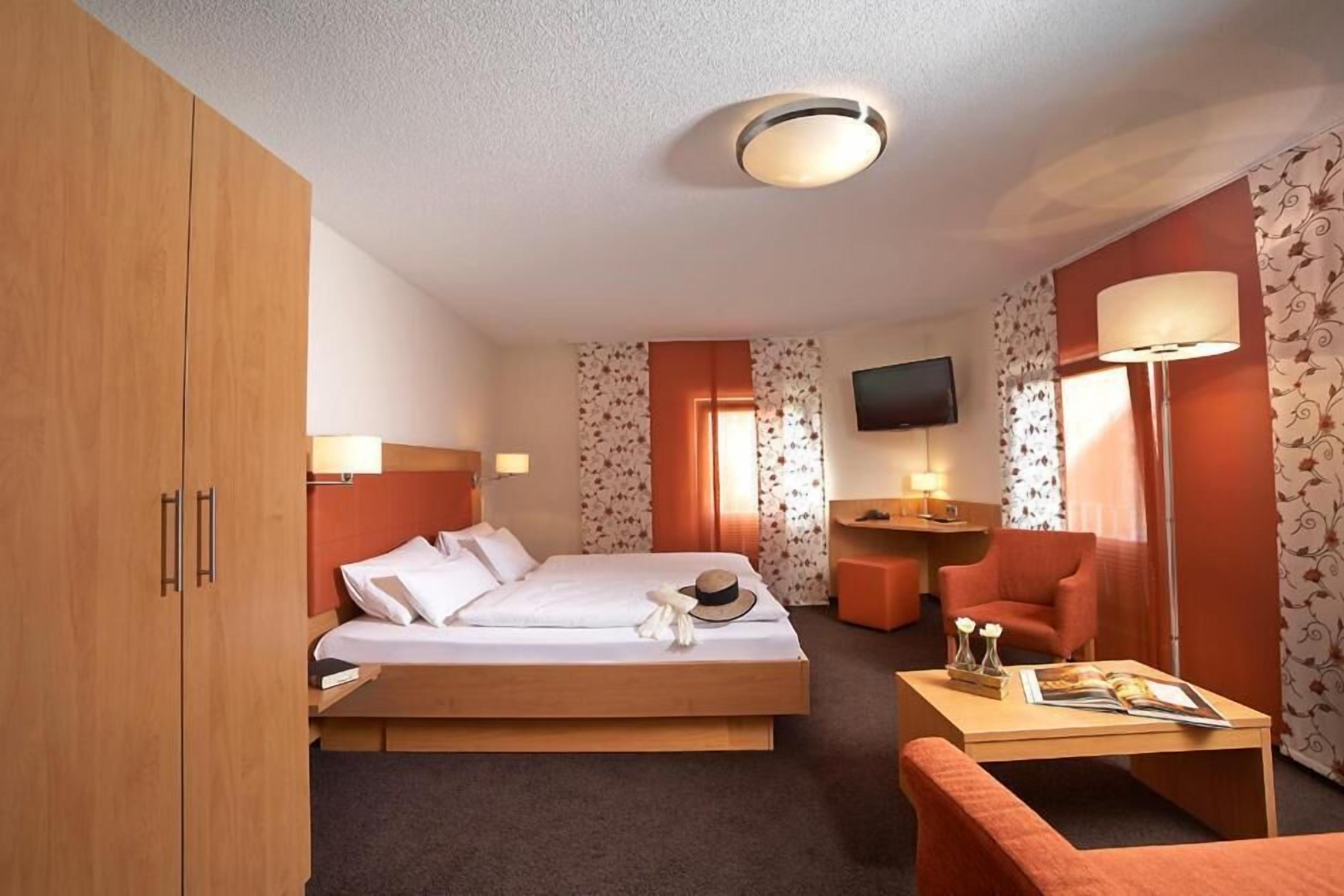 Habitación de hotel con una cama, un escritorio, una silla, un televisor y un armario.