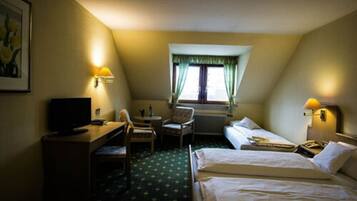 Une chambre d’hôtel équipée d’un bureau, d’une chaise, de deux lits, d’un radiateur et d’une fenêtre avec des rideaux.
