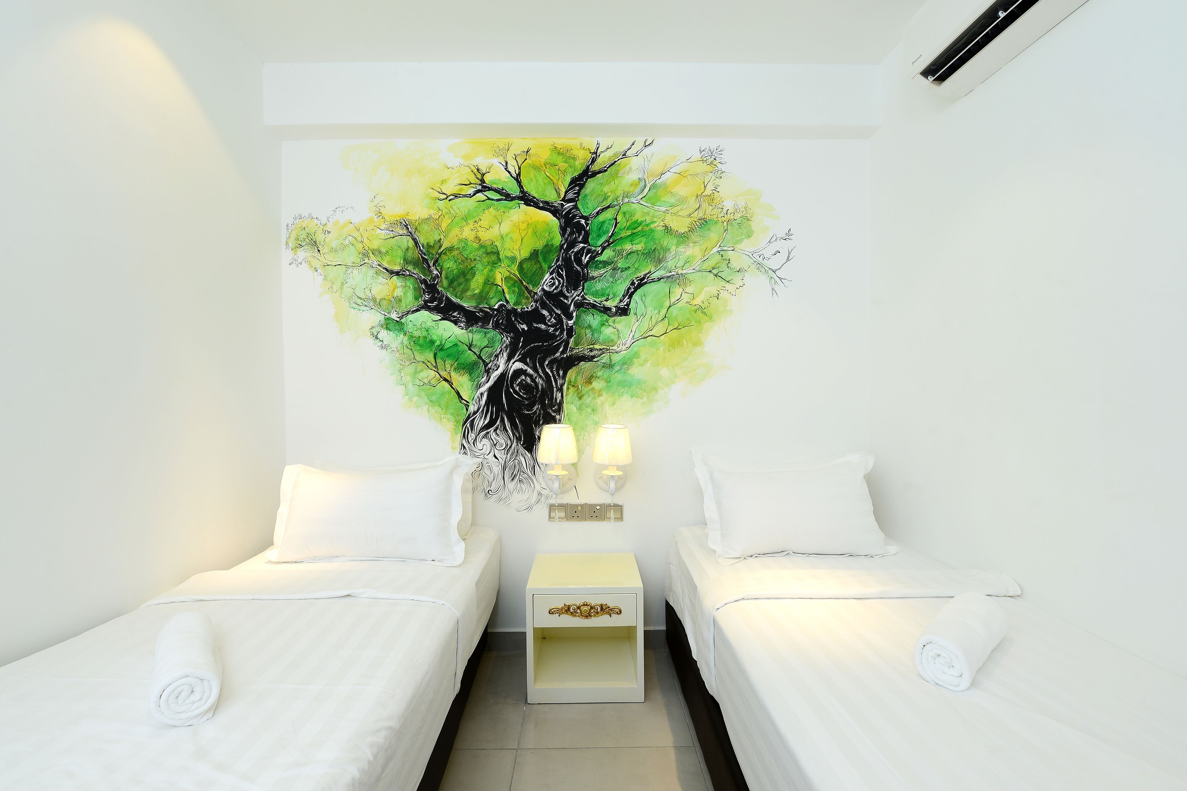 A hotel room with two beds, a nightstand, and a wall-mounted painting of a tree.