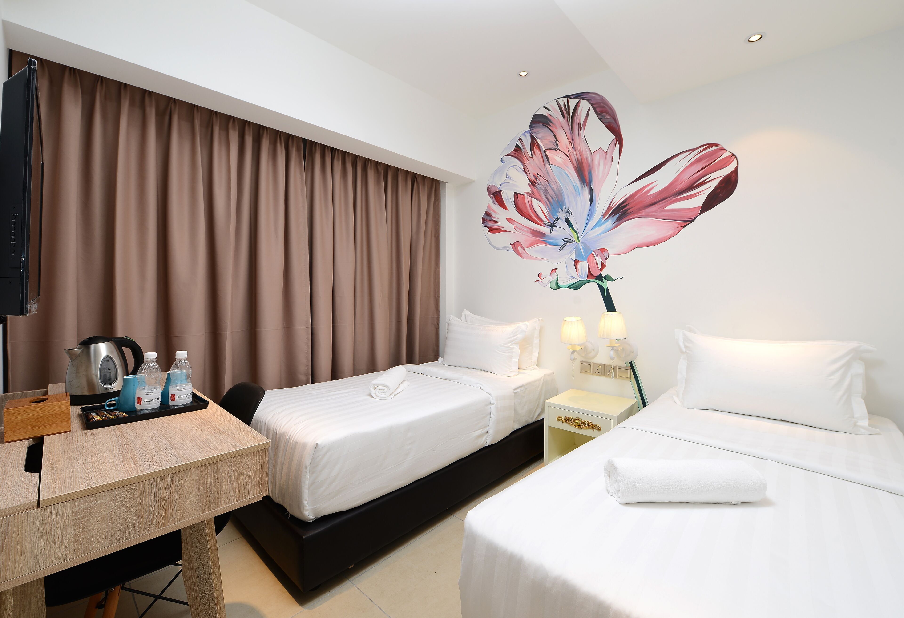 A hotel room with two beds, a desk, a TV, and a large floral mural on the wall.