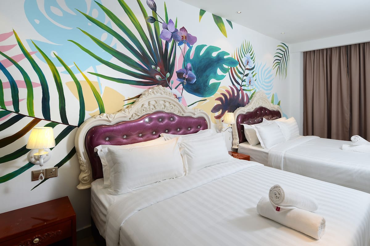 Une chambre d’hôtel avec deux lits, une fresque murale décorative et un rideau marron.